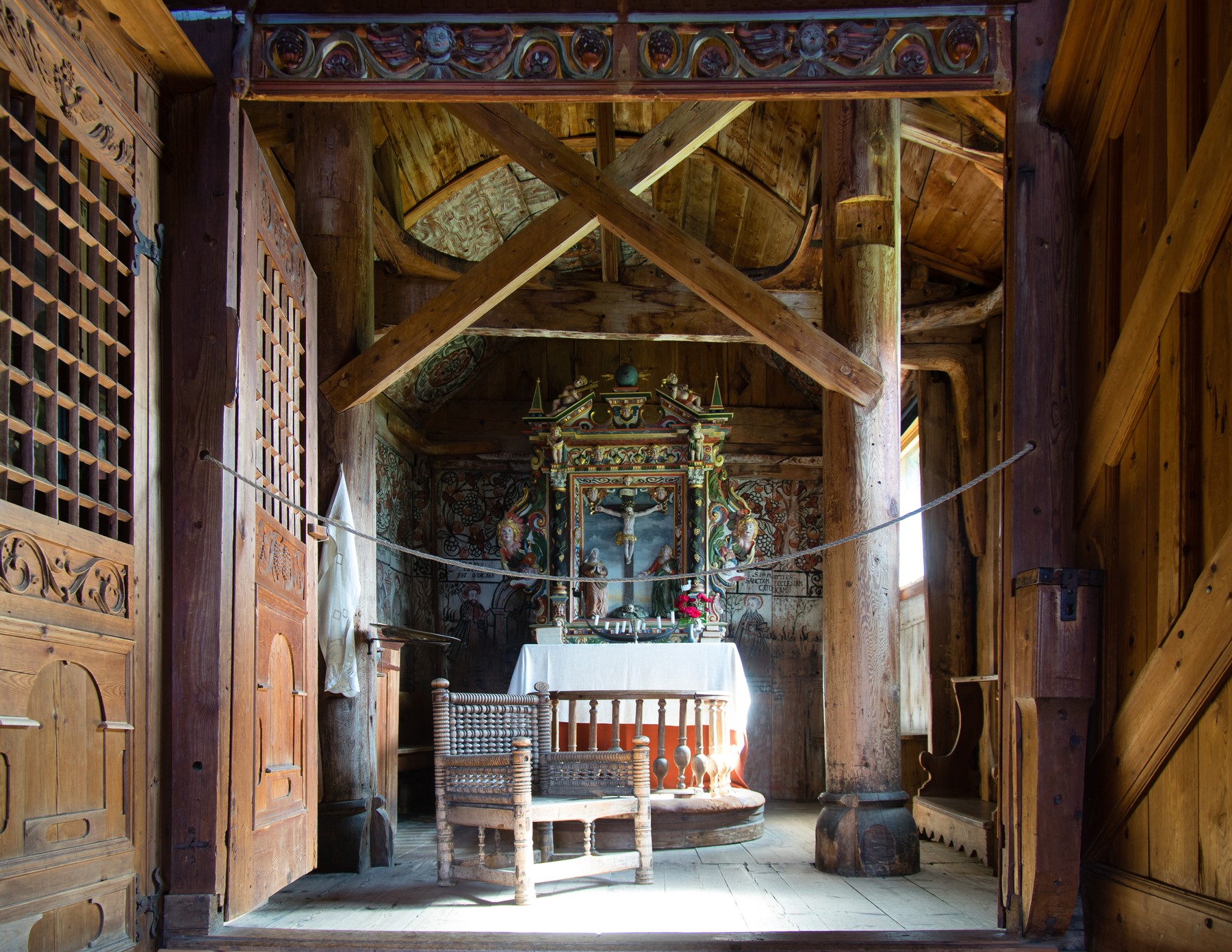 Upright timbers, crossing diagonal bracing and curved members above furnishings inside Urnes stave church.