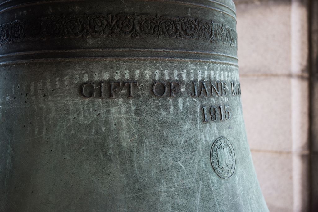 Close view of a bronze bell shows part of a raised gift inscription, the date 1915 and a small foundry emblem.