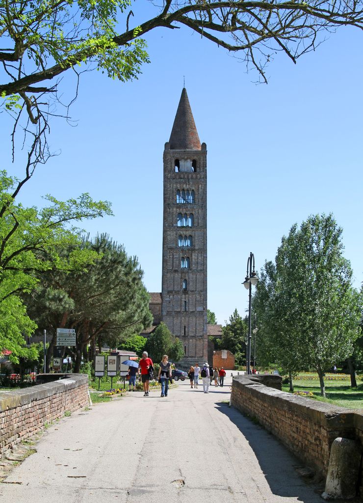 A tall square brick tower with a conical top rises above an approach path; its windows become broader toward the top.