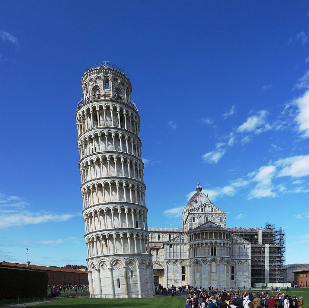 The leaning arcaded tower stands beside the cathedral’s apse and dome, with visitors at ground level.