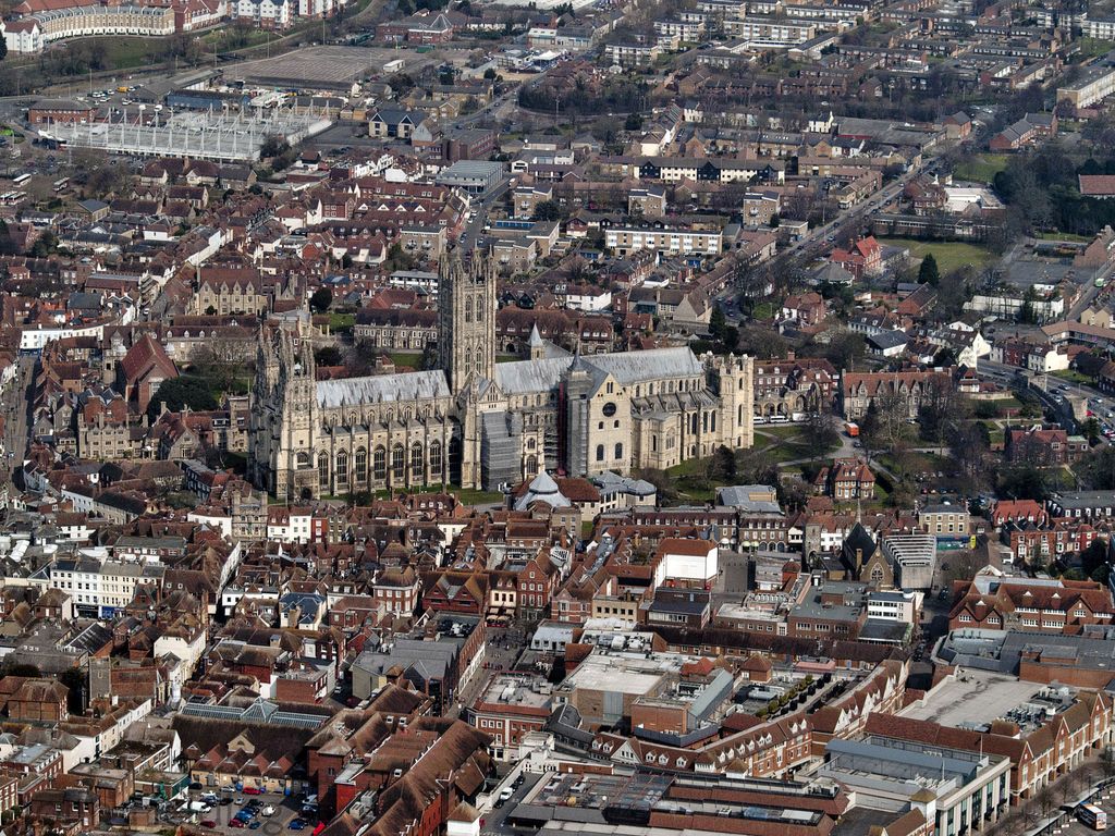An elongated cathedral with west towers, a tall central tower and successive eastern roofs stands among streets and surrounding precinct buildings.
