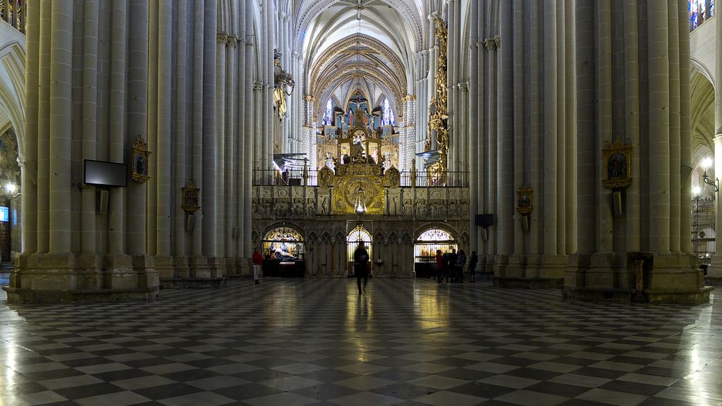 A broad carved choir enclosure stands between enormous nave piers, with three lower openings, side passages and the cathedral vaults above.