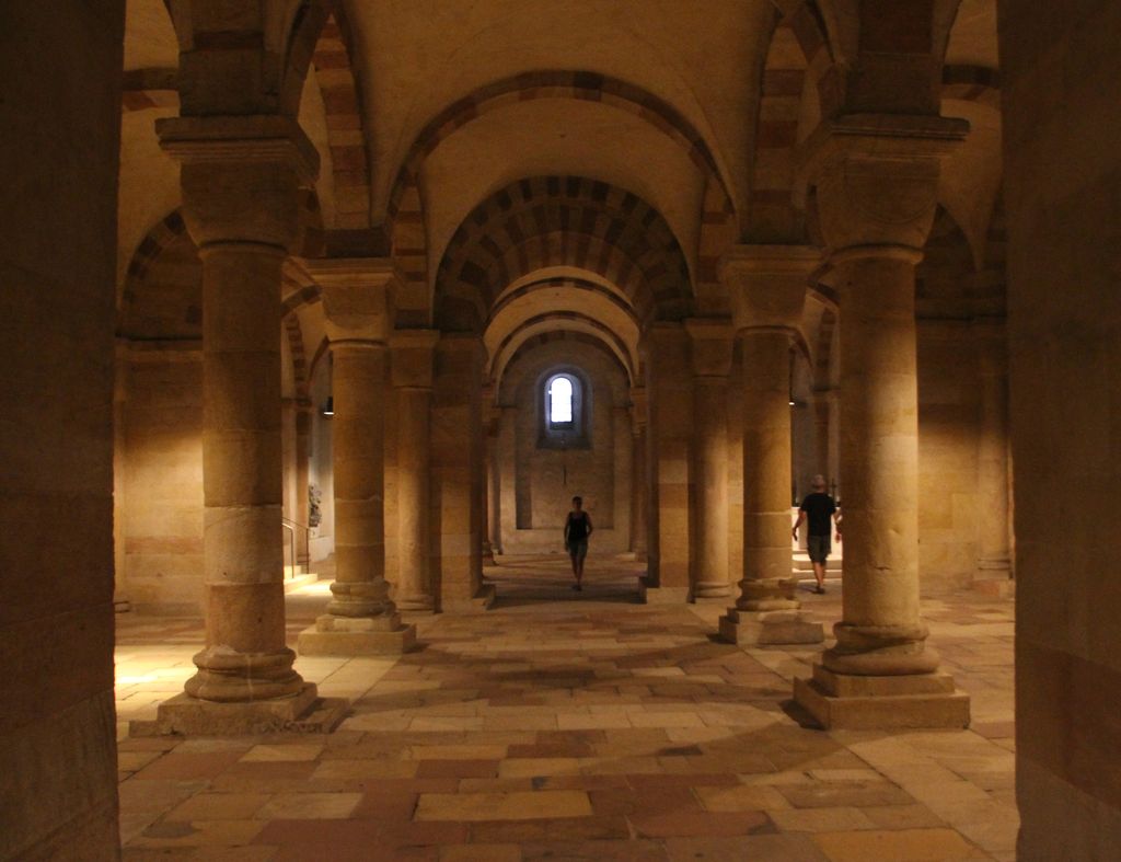 Rows of round columns with cushion capitals divide a broad stone-floored hall beneath banded arches and groined vaults.