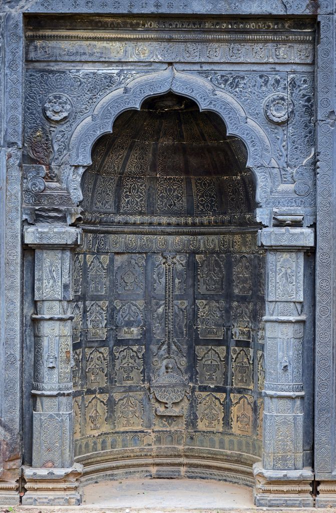 A scalloped carved stone arch frames a curved niche with a large hanging lamp depicted in relief at its centre.