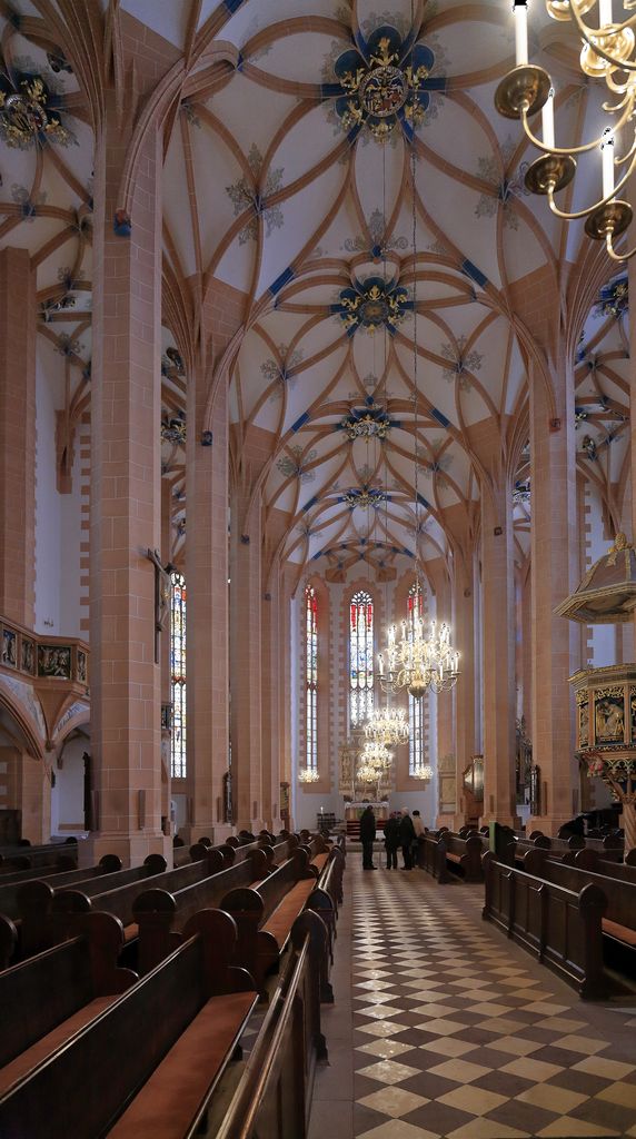 Tall slender piers support looping ribs across adjoining vaulted spaces, while pews flank a central walking aisle toward the choir.