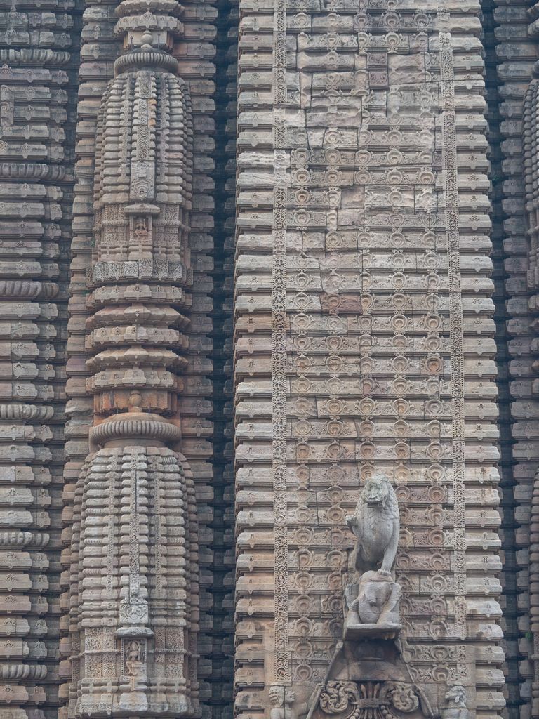 Carved vertical stone bands carry rows of scroll motifs and small shrine-like forms, with a lion projecting at the lower right.