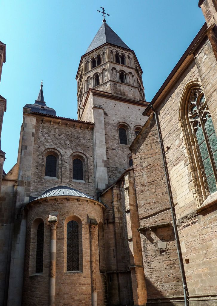 A rounded chapel apse stands below tall transept masonry and an octagonal tower, beside a wall with a pointed traceried window.