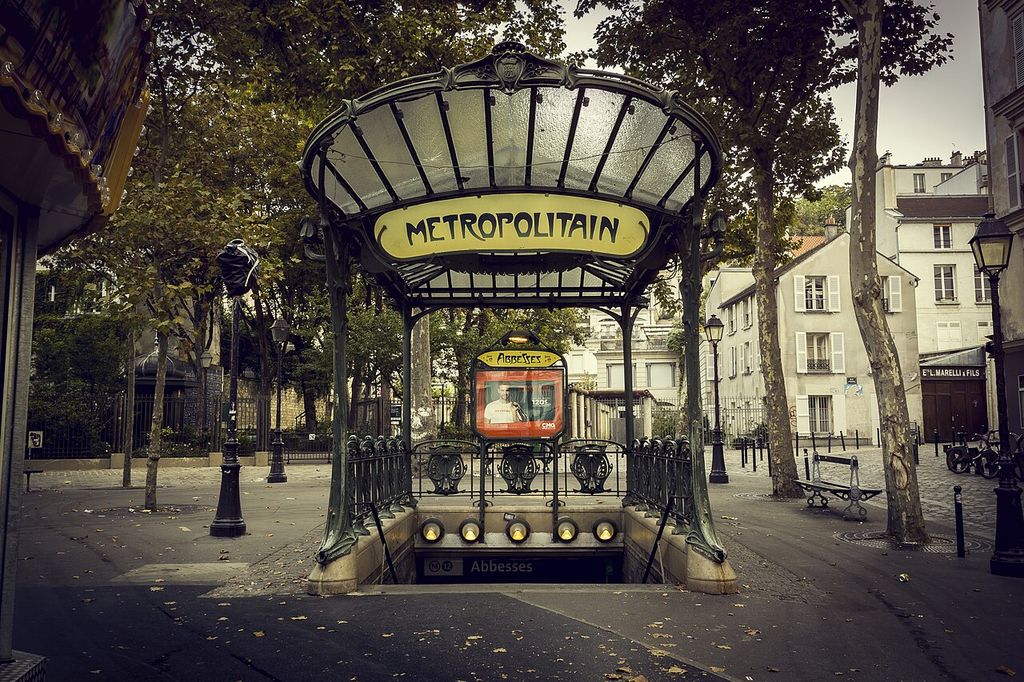 Curved metal supports carry a glazed canopy and Métropolitain sign above railings and descending stairs.