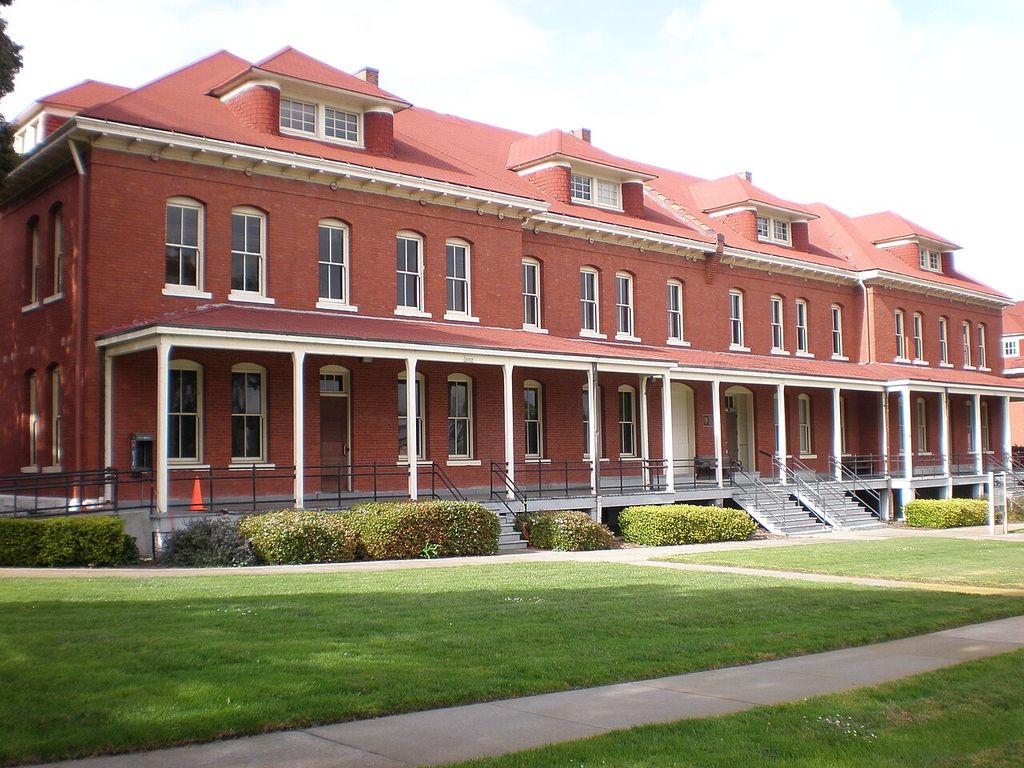 A long red-brick barracks has repeated sash windows, dormers and a continuous white-painted veranda.
