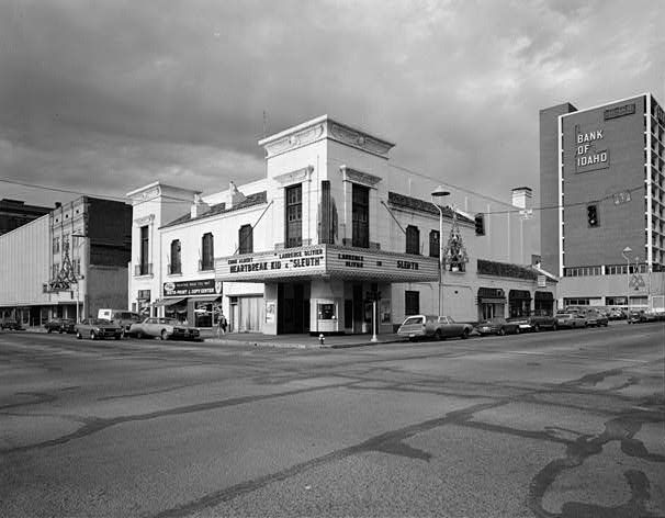 A corner cinema has tall pylon-like sections above a projecting marquee, with cars along the surrounding streets.