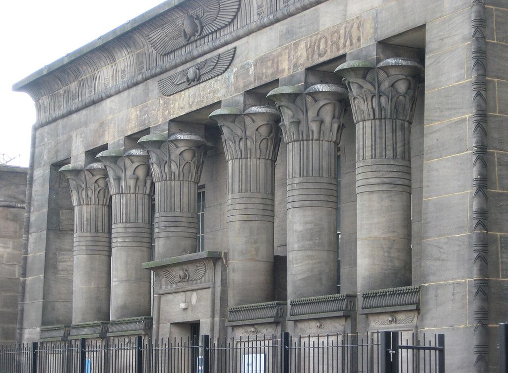 Large columns with plant capitals stand beneath a concave cornice and winged decorative symbols.