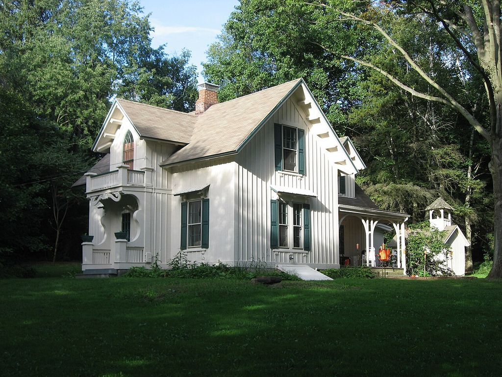 A pale timber house has steep gables, a pointed upper window and shaped wooden porch brackets.