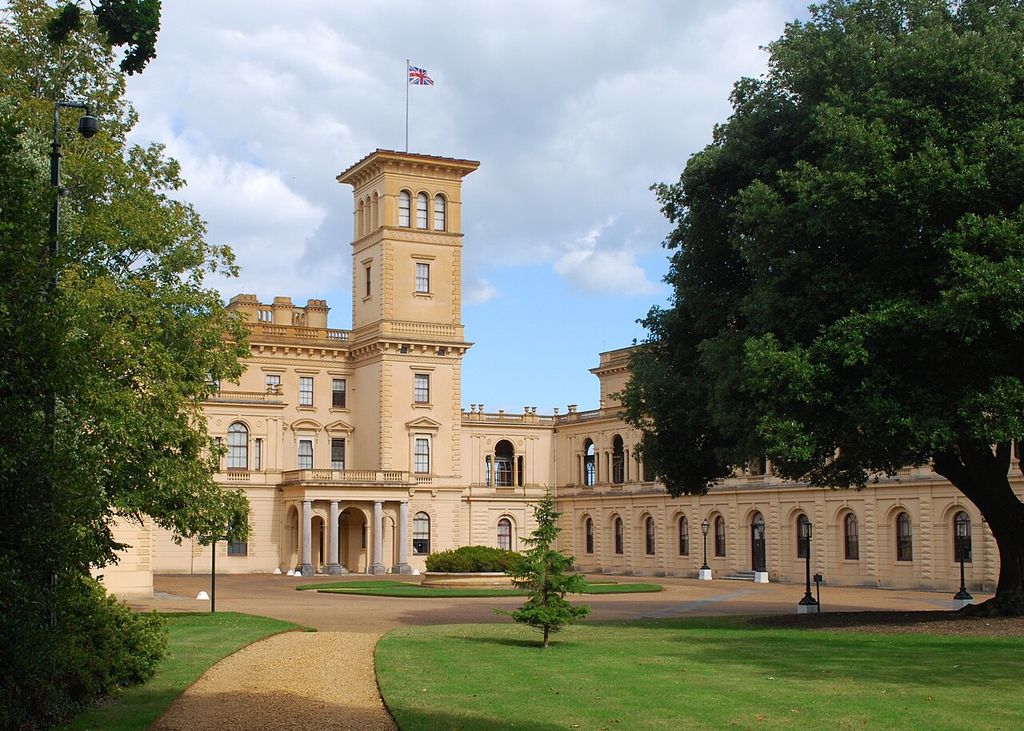 A tall Italianate tower rises behind a columned entrance and ranges around a forecourt.