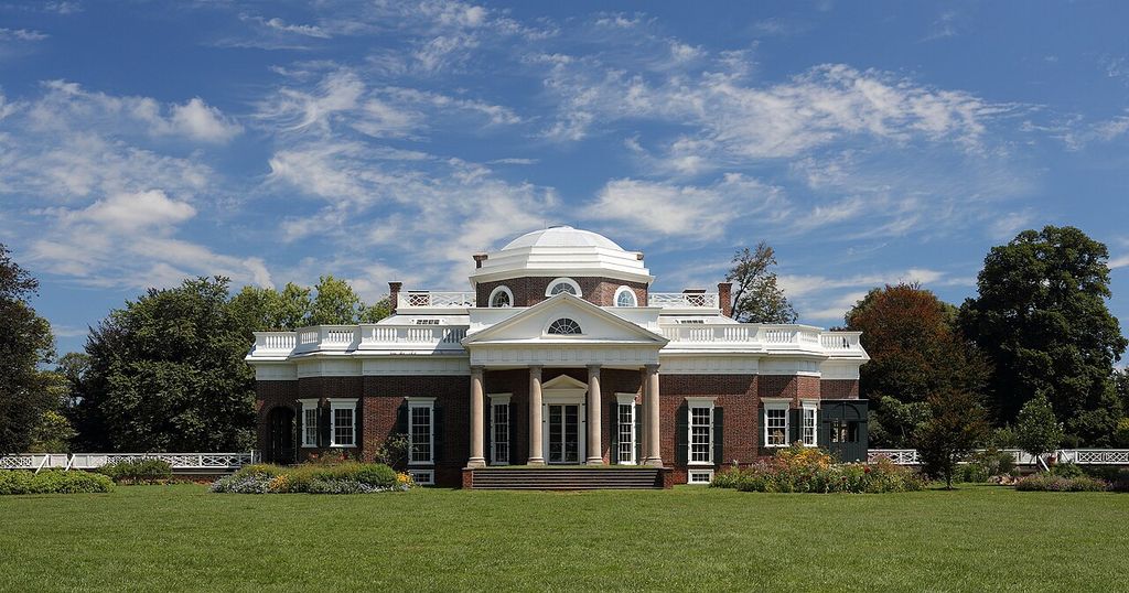 Brick house with a central columned portico, pediment and low dome, with terraces extending to either side.