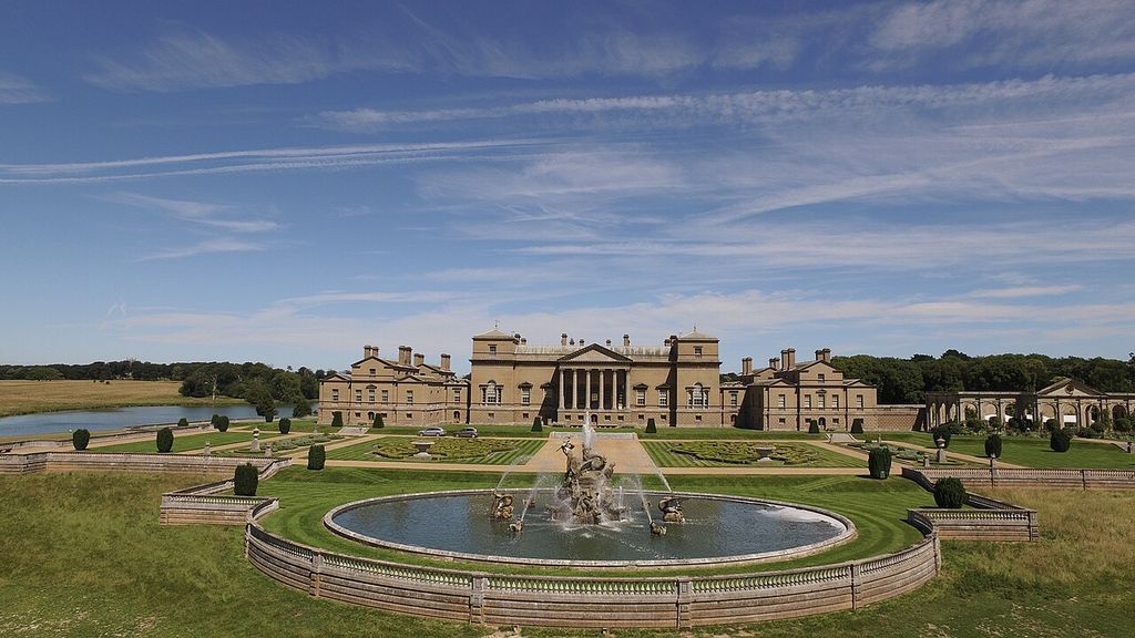 A large central porticoed block is balanced by lower ranges beyond a formal garden and fountain.