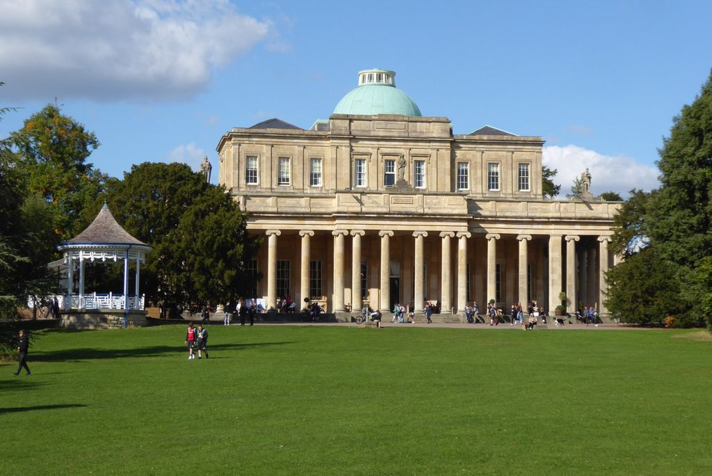 An Ionic colonnade fronts a symmetrical stone building with a central dome, viewed across a lawn.