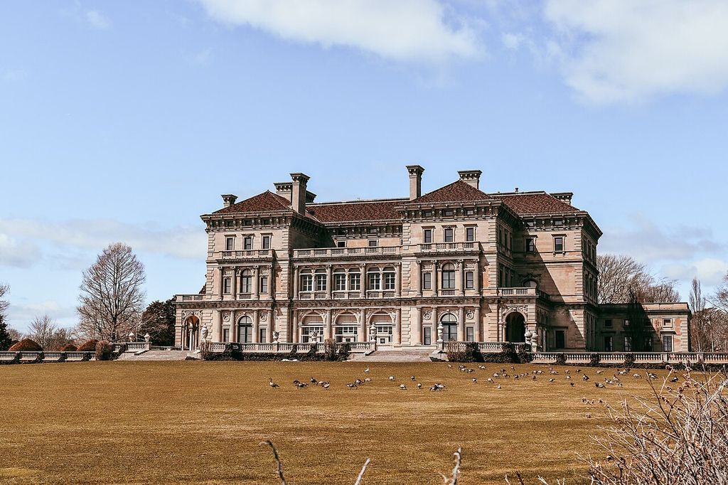 A large mansion combines columned loggias, ranked windows, balustrades and prominent cornices above a broad lawn.