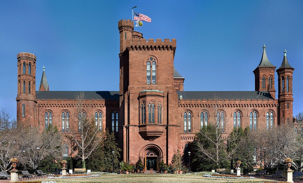 Red masonry walls and round-headed windows link towers of different shapes and heights.