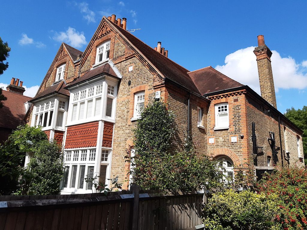 Brick houses with paired gables, white projecting windows, red tile hanging and tall chimneys behind garden shrubs.