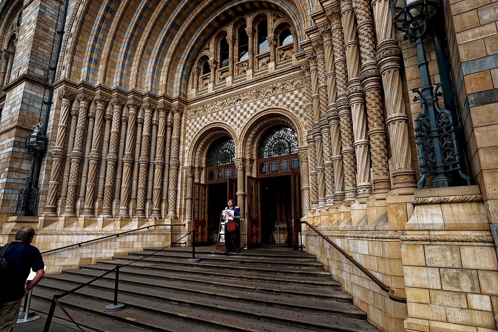 Nested round arches, decorated shafts and alternating pale and blue-grey terracotta frame a museum entrance.