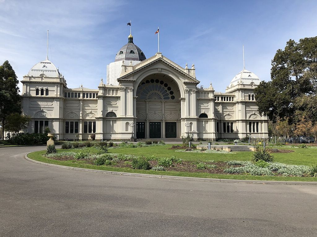 A monumental round-arched entrance and domed pavilions face a garden, with protective sheeting on the central dome drum.