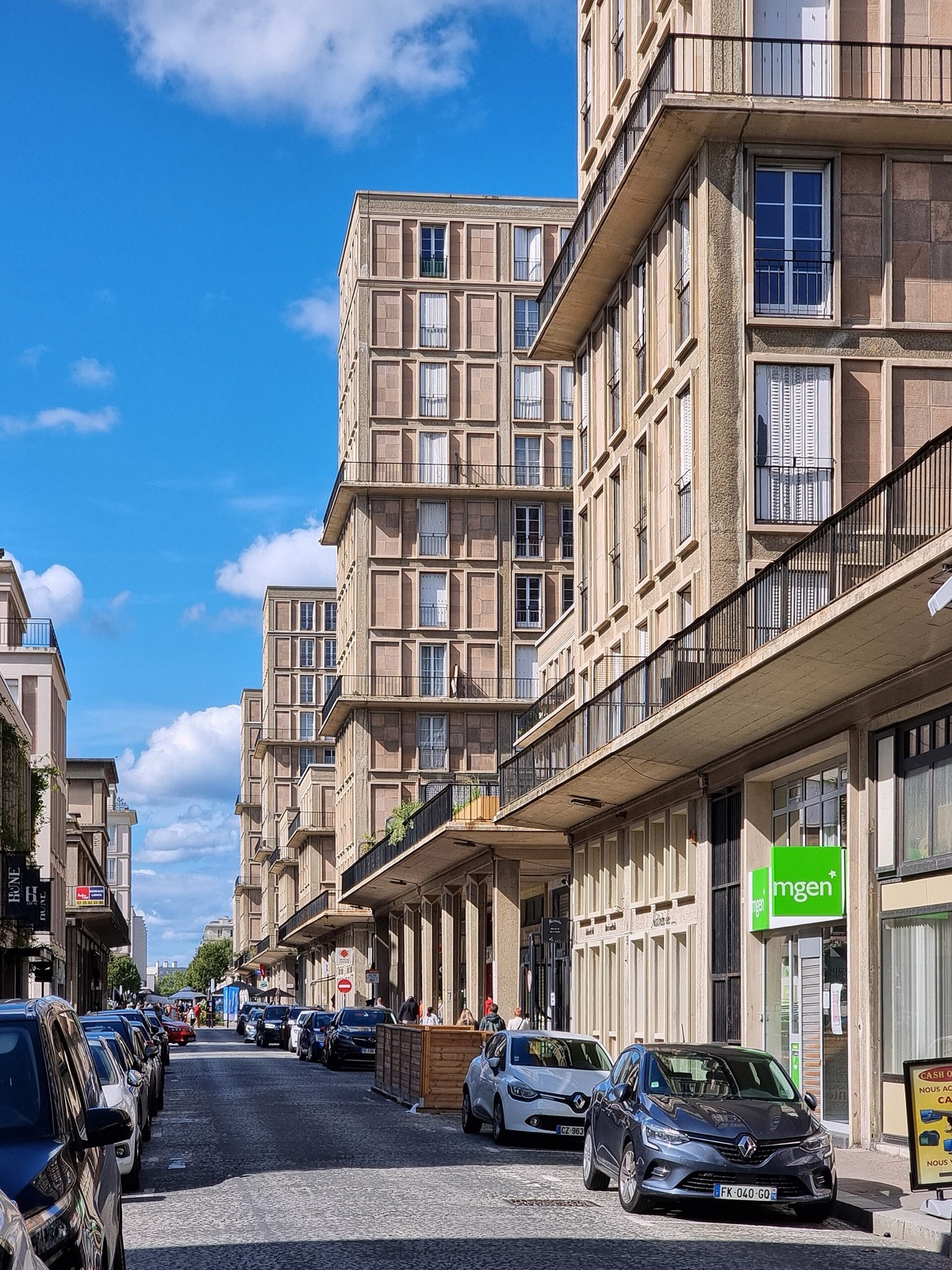 Perret-era Le Havre street with concrete bay rhythm across varied apartment fronts and ground-level shops.