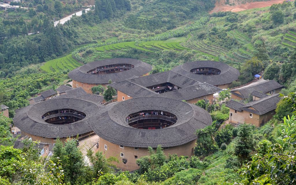 Four round or oval and one square earth-walled compounds cluster among steep green cultivated hills.