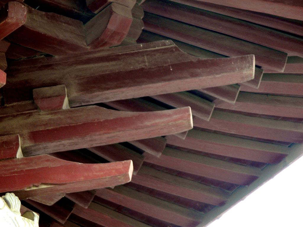 Red-painted timber bracket arms project in overlapping layers beneath dark roof members and tiles.