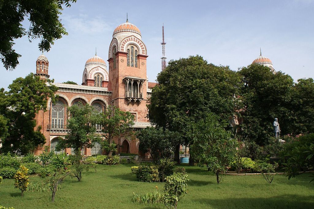 Domed towers and tall arched windows rise above a garden, with trees partly obscuring the lower and right-hand facade.