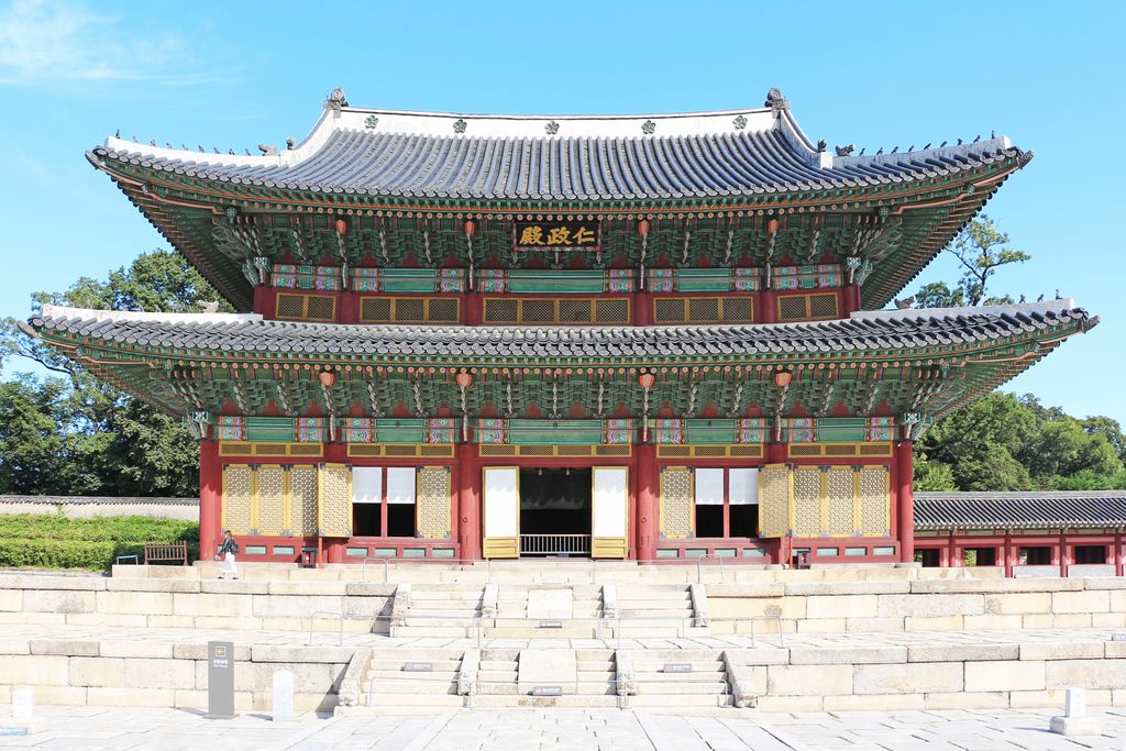 A richly painted two-storey timber hall with grey tiled roofs stands on a broad pale stone platform.