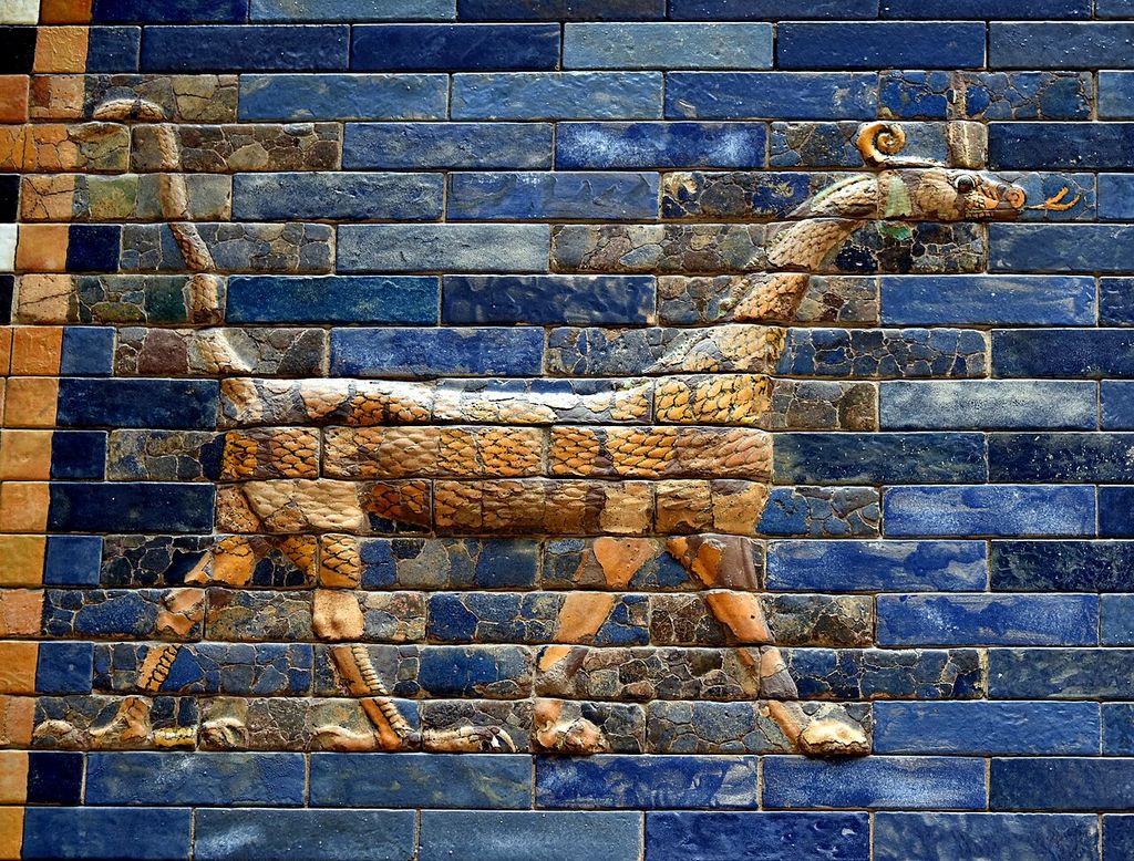 A long horned dragon in cream, gold and brown glazed relief bricks walks across a wall of deep blue rectangular bricks.