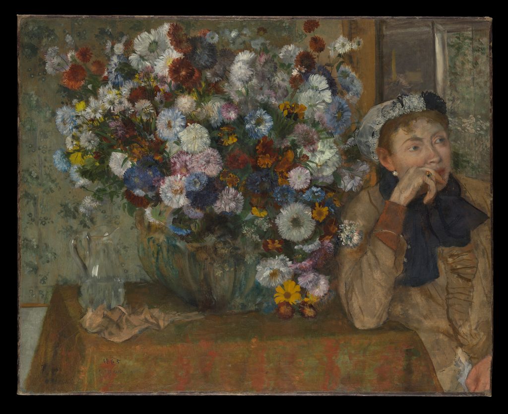 Woman seated beside a tall vase of flowers, her face partly hidden by the arrangement