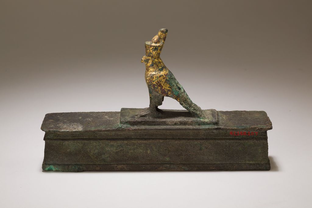 A gilded falcon wearing Egypt's double crown stands above a shrine-shaped animal-mummy box.