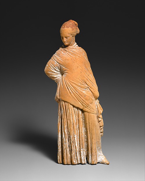 Small Greek terracotta woman standing in layered drapery and a broad hat.