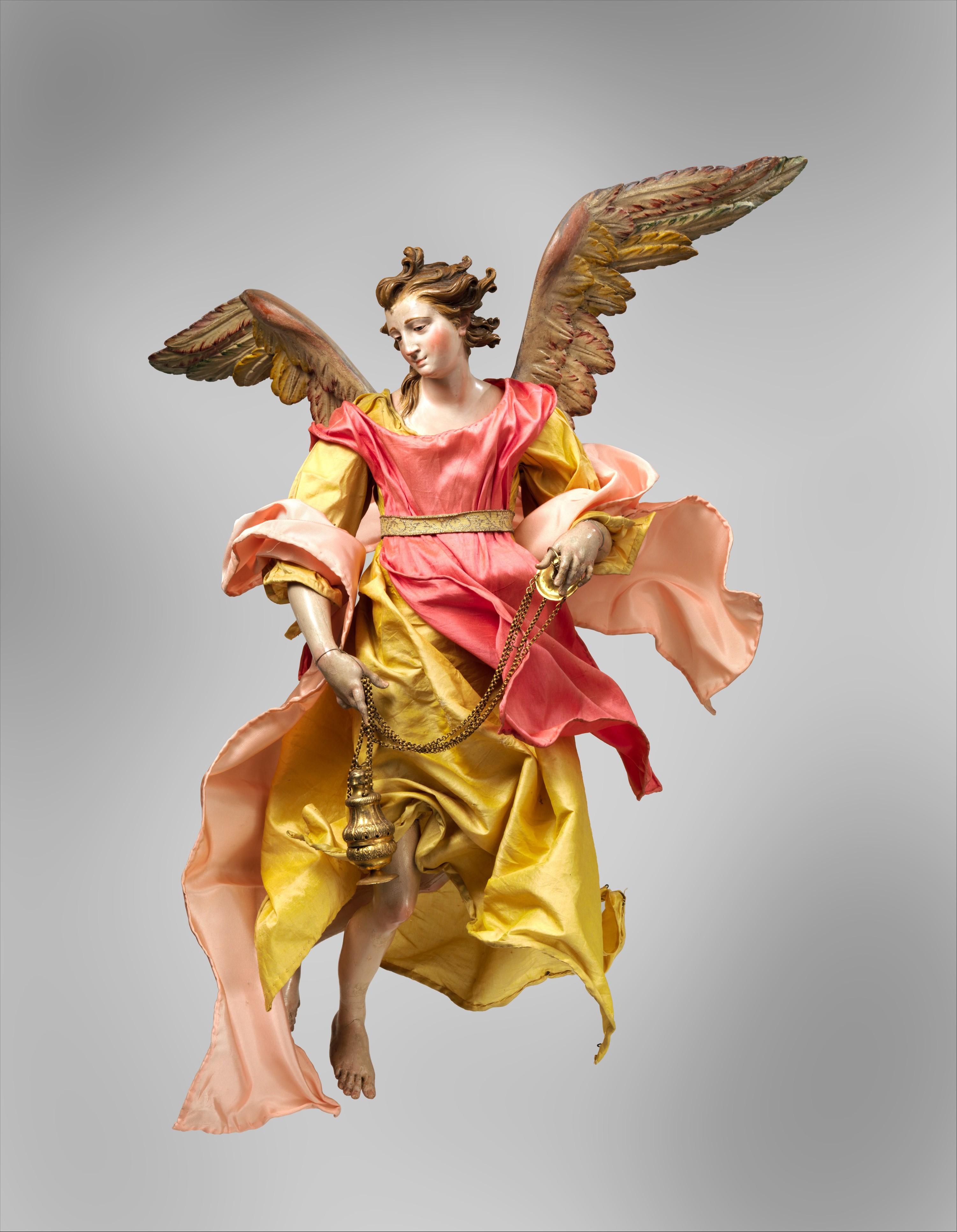Polychromed crèche angel with outspread wings, flowing pink and yellow fabrics and articulated wooden limbs around a wire-and-tow body.